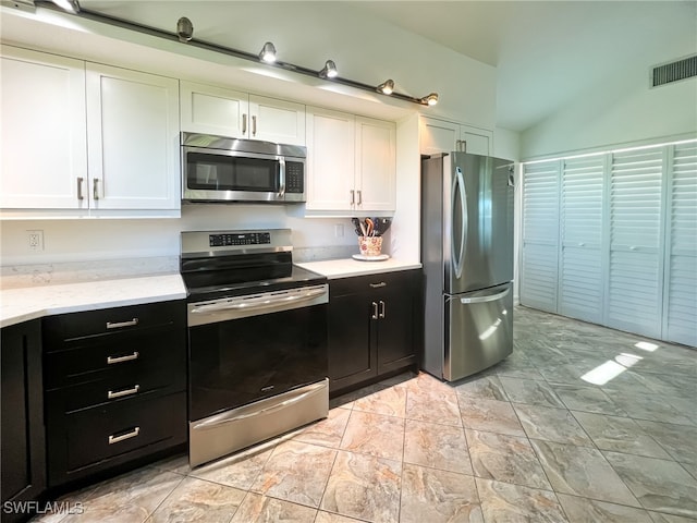 kitchen featuring light stone counters, white cabinets, stainless steel appliances, and lofted ceiling