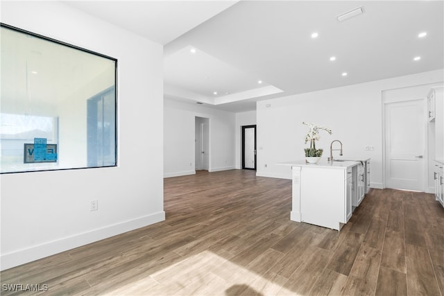 kitchen with white cabinets, wood-type flooring, a center island with sink, and sink