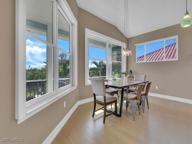 dining room with light wood-type flooring, vaulted ceiling, and plenty of natural light