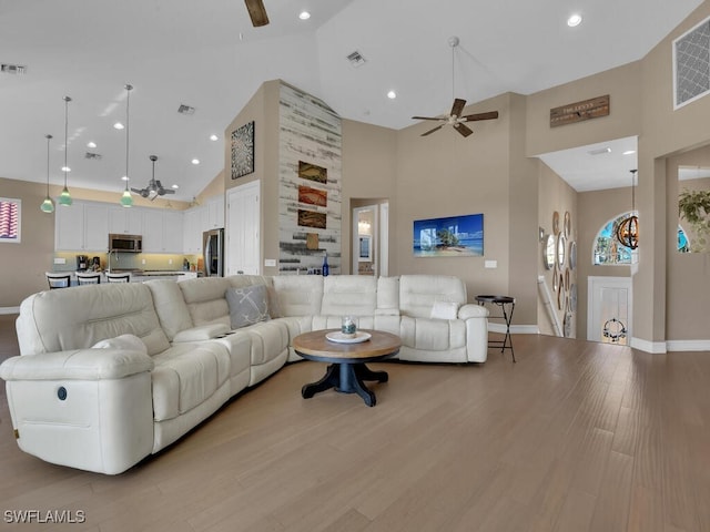 living room featuring ceiling fan, high vaulted ceiling, and light hardwood / wood-style flooring