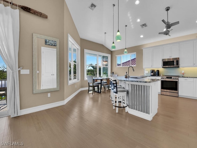 kitchen with light wood-type flooring, stainless steel appliances, pendant lighting, white cabinetry, and an island with sink