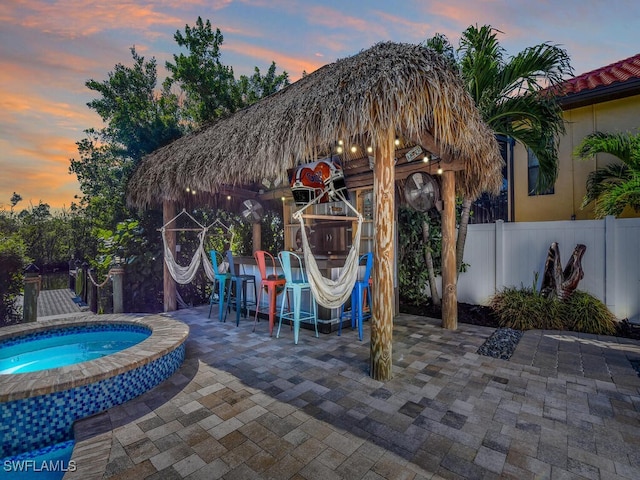 pool at dusk with exterior bar, an in ground hot tub, and a patio area