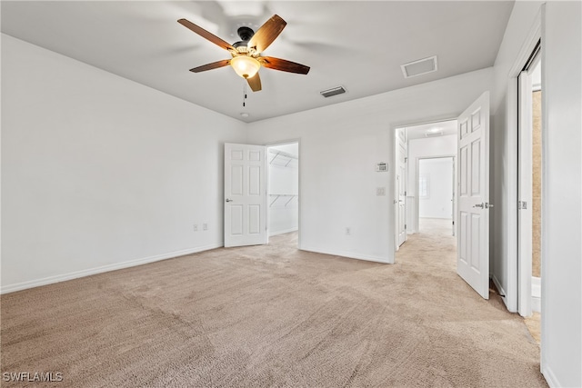 unfurnished bedroom with a walk in closet, ceiling fan, a closet, and light colored carpet