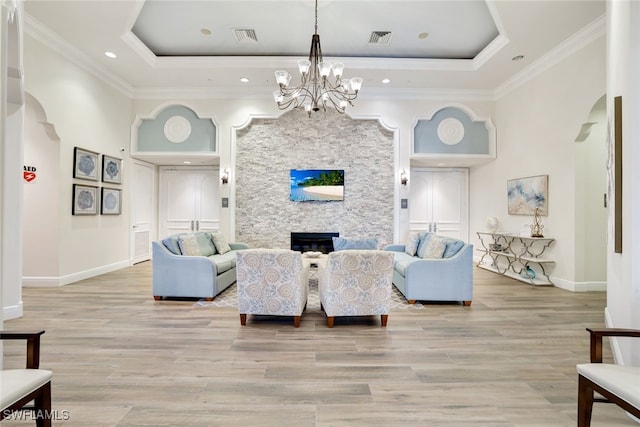 living room with a stone fireplace, a notable chandelier, a tray ceiling, light hardwood / wood-style flooring, and crown molding