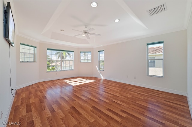 empty room featuring light wood-type flooring, visible vents, baseboards, crown molding, and a raised ceiling