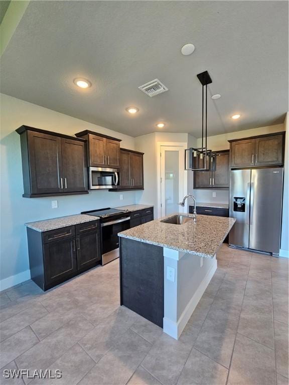 kitchen featuring appliances with stainless steel finishes, light stone counters, a kitchen island with sink, sink, and decorative light fixtures