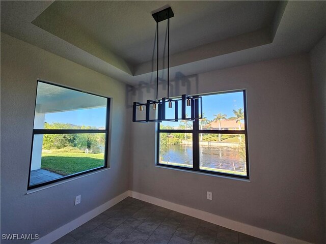 unfurnished dining area featuring a water view, a wealth of natural light, and a tray ceiling