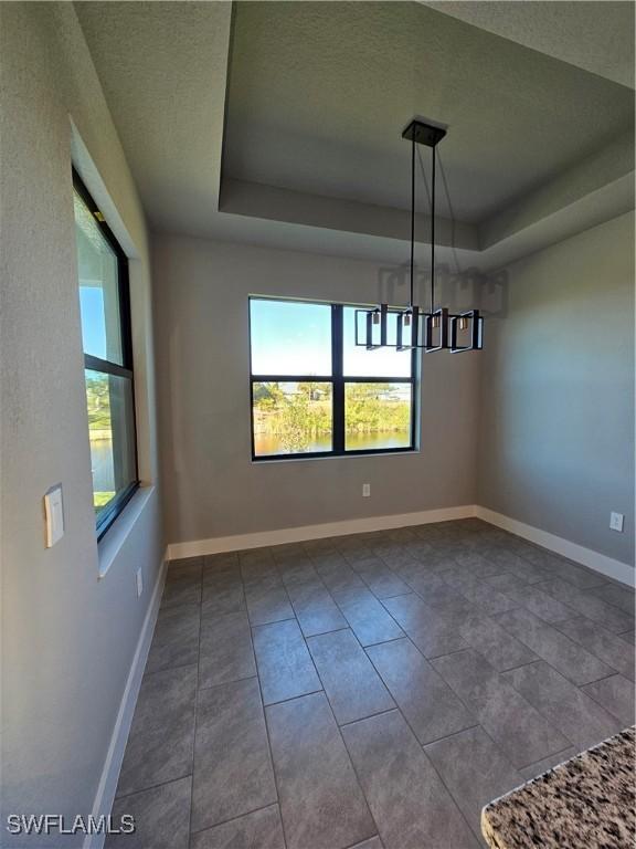 unfurnished dining area with tile patterned flooring, a healthy amount of sunlight, a textured ceiling, and an inviting chandelier