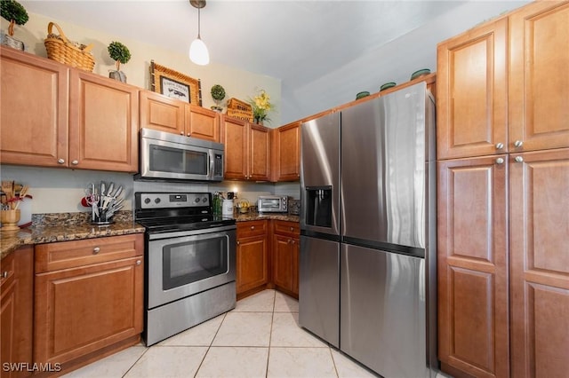 kitchen with dark stone countertops, light tile patterned floors, stainless steel appliances, and decorative light fixtures