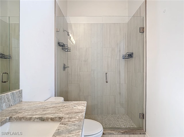 bathroom featuring a shower with door, vanity, and toilet