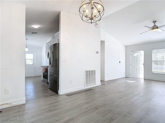 unfurnished living room featuring ceiling fan with notable chandelier, vaulted ceiling, and light wood-type flooring