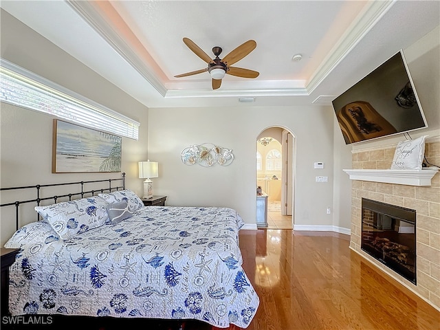 bedroom featuring a tray ceiling, a tiled fireplace, ceiling fan, and hardwood / wood-style floors