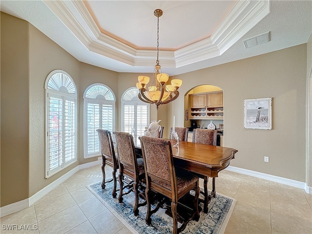 tiled dining room with ornamental molding, a tray ceiling, and an inviting chandelier