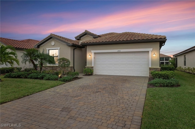 view of front of home with decorative driveway, stucco siding, stone siding, a garage, and a front yard