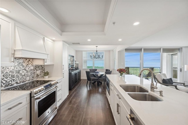 kitchen with custom range hood, sink, electric range, decorative light fixtures, and white cabinetry