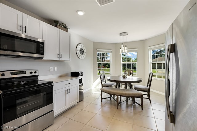 kitchen featuring appliances with stainless steel finishes, decorative light fixtures, an inviting chandelier, white cabinets, and light tile patterned flooring