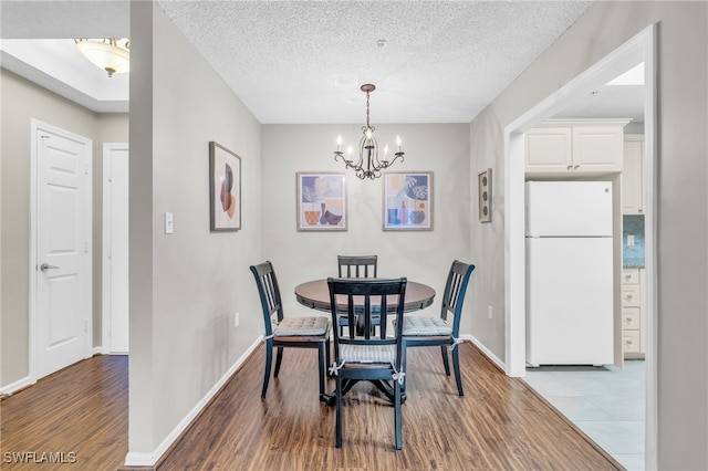 dining space with a textured ceiling, baseboards, wood finished floors, and an inviting chandelier