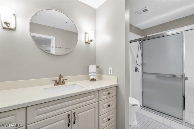 bathroom featuring tile patterned flooring, vanity, toilet, a shower with door, and a textured ceiling