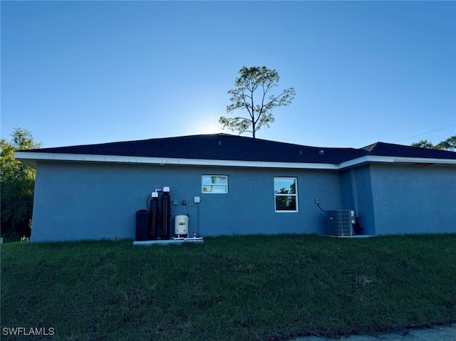 rear view of property with central air condition unit and a yard