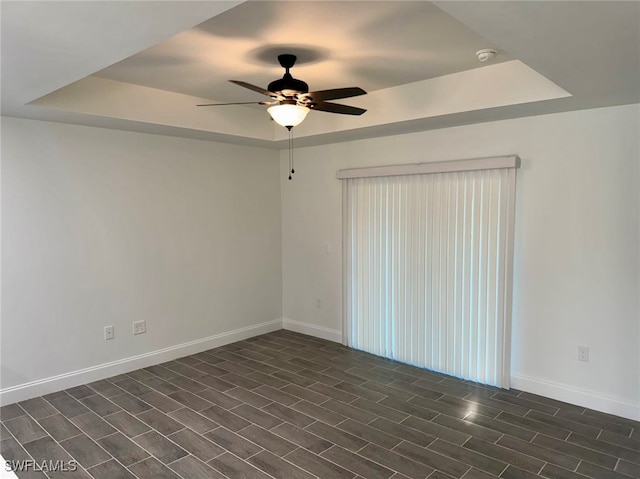 empty room with ceiling fan, a raised ceiling, and dark wood-type flooring