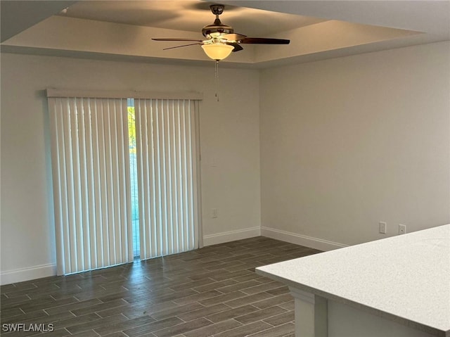 spare room with a raised ceiling, ceiling fan, and dark hardwood / wood-style floors