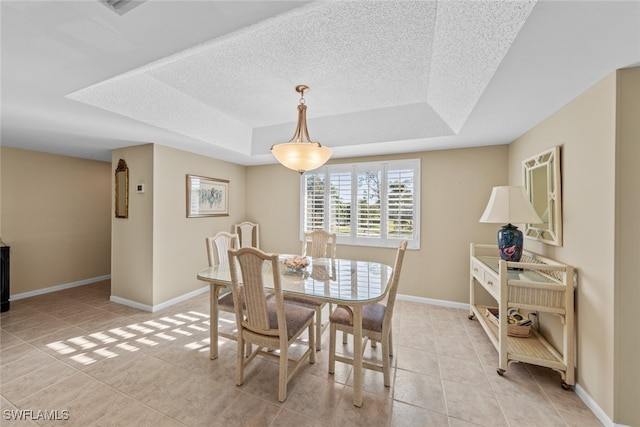 tiled dining space with a textured ceiling and a tray ceiling