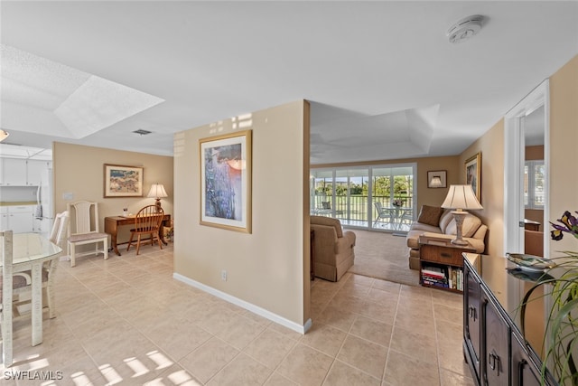 hallway featuring a tray ceiling and light tile patterned floors