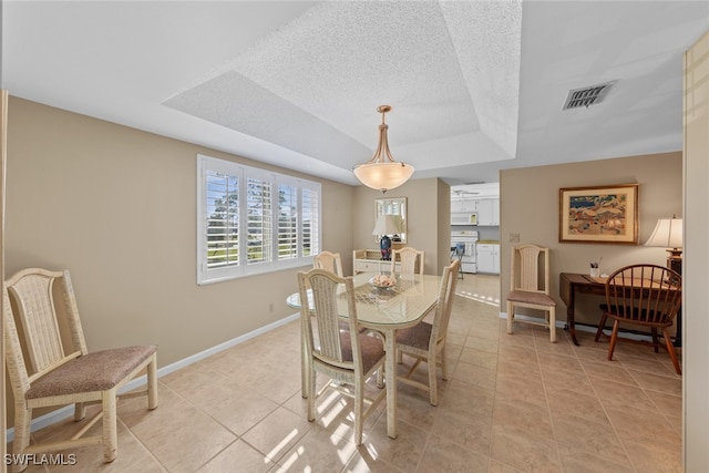 tiled dining area with a textured ceiling and a tray ceiling