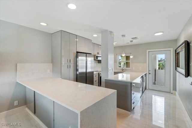 kitchen with hanging light fixtures, gray cabinets, stainless steel fridge, tasteful backsplash, and kitchen peninsula