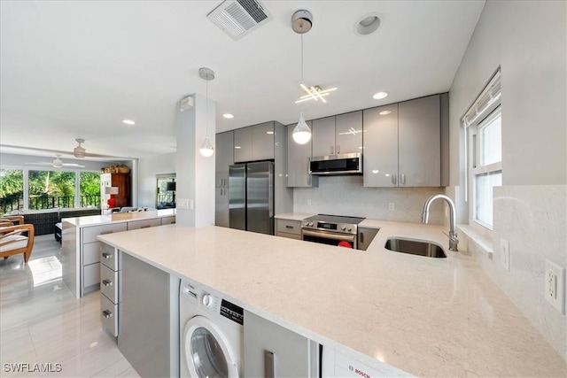 kitchen with sink, hanging light fixtures, kitchen peninsula, washer / clothes dryer, and appliances with stainless steel finishes