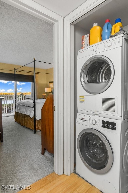 laundry room with a textured ceiling, stacked washer / dryer, and hardwood / wood-style floors