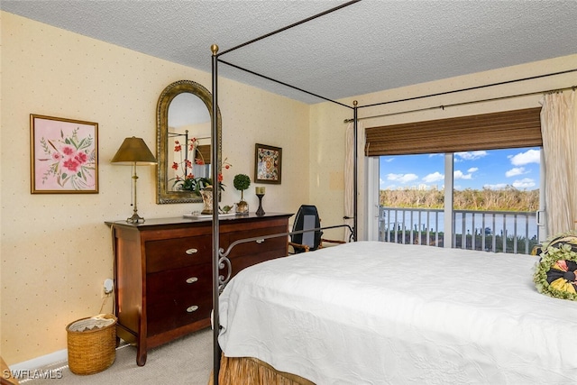 bedroom featuring access to outside, a water view, carpet, and a textured ceiling