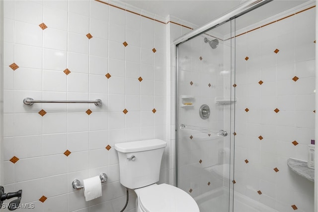 bathroom with toilet, a shower with shower door, and tile walls