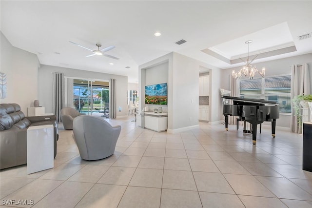 living room with light tile patterned floors, ceiling fan with notable chandelier, and a raised ceiling