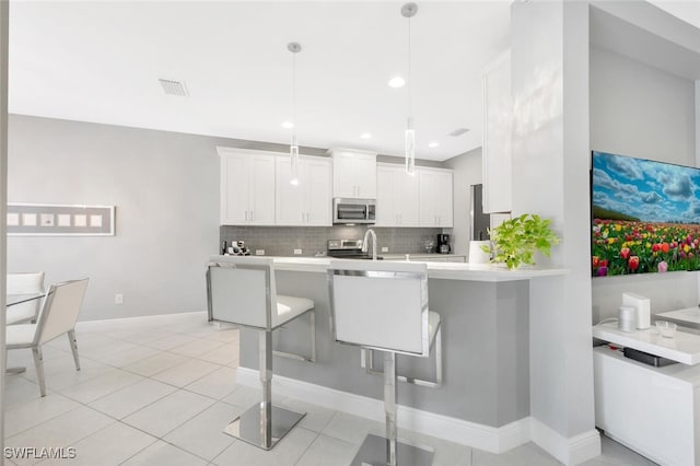 kitchen featuring kitchen peninsula, a kitchen bar, light tile patterned floors, white cabinets, and hanging light fixtures