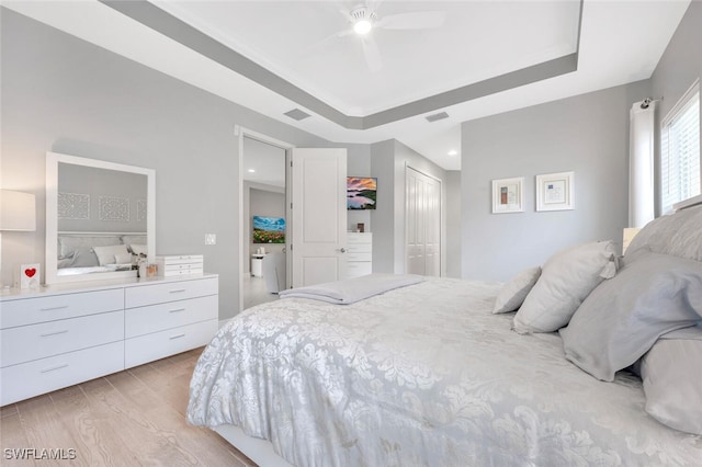 bedroom featuring ceiling fan, light hardwood / wood-style floors, a raised ceiling, and a closet