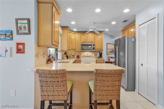 kitchen with sink, kitchen peninsula, a kitchen bar, light brown cabinetry, and appliances with stainless steel finishes