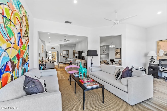 living room with ceiling fan with notable chandelier and light hardwood / wood-style floors