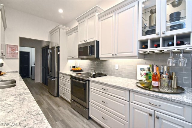 kitchen featuring white cabinets, tasteful backsplash, glass insert cabinets, and stainless steel appliances