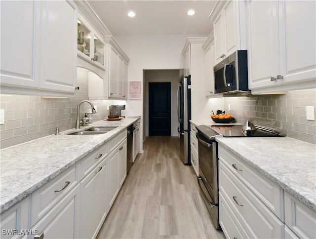 kitchen featuring glass insert cabinets, appliances with stainless steel finishes, light stone countertops, white cabinetry, and a sink