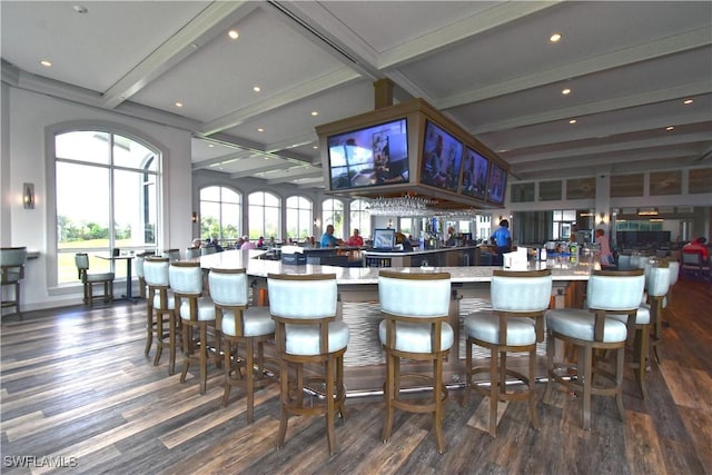 bar featuring dark wood-style floors, beamed ceiling, and a community bar