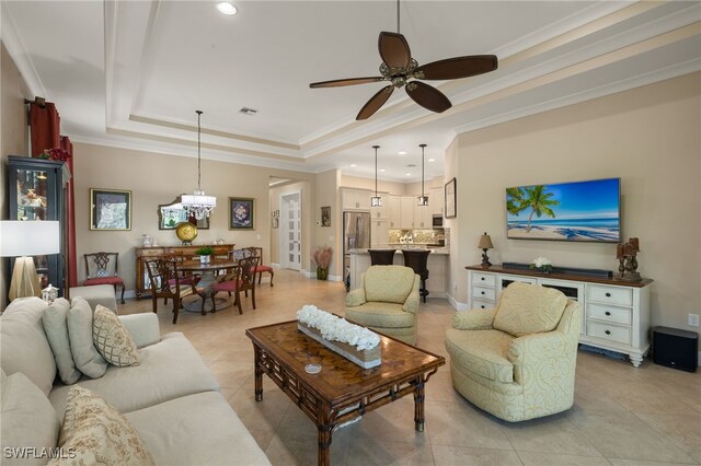 living room with crown molding, a tray ceiling, ceiling fan with notable chandelier, and light tile patterned floors