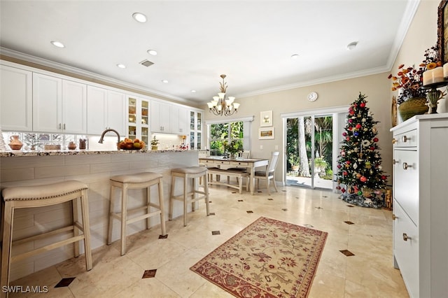 kitchen with light stone countertops, white cabinetry, a breakfast bar area, and ornamental molding