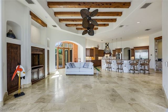 unfurnished living room with ceiling fan, a towering ceiling, and beamed ceiling