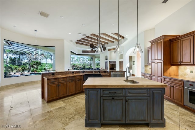 kitchen with beamed ceiling, decorative light fixtures, stainless steel oven, and a kitchen island with sink