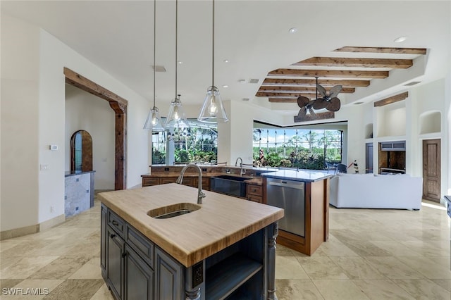 kitchen featuring stainless steel dishwasher, sink, a kitchen island with sink, and beamed ceiling