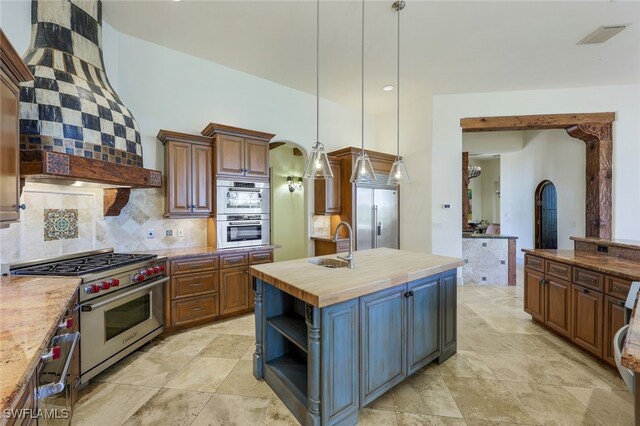 kitchen featuring high quality appliances, a kitchen island with sink, sink, butcher block countertops, and custom range hood