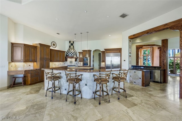 kitchen with a kitchen bar, appliances with stainless steel finishes, stone countertops, decorative light fixtures, and a large island