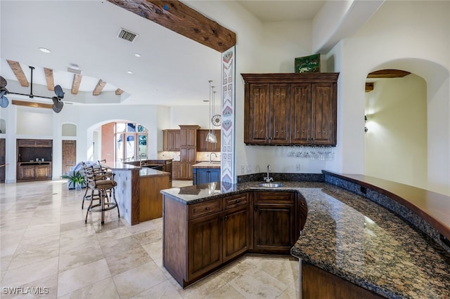 kitchen featuring kitchen peninsula, dark stone counters, dark brown cabinets, sink, and beamed ceiling