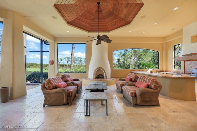 living room with a tray ceiling, a wealth of natural light, ceiling fan, and wood ceiling